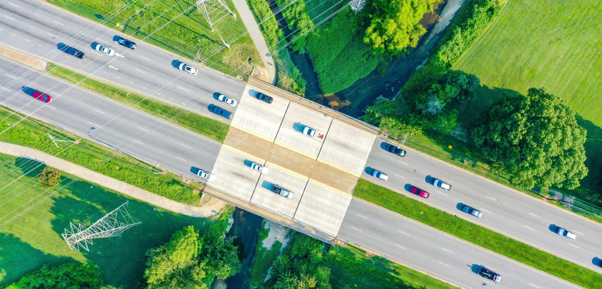 an aerial view of a bridge over the creek and powerlines with cars on the road
